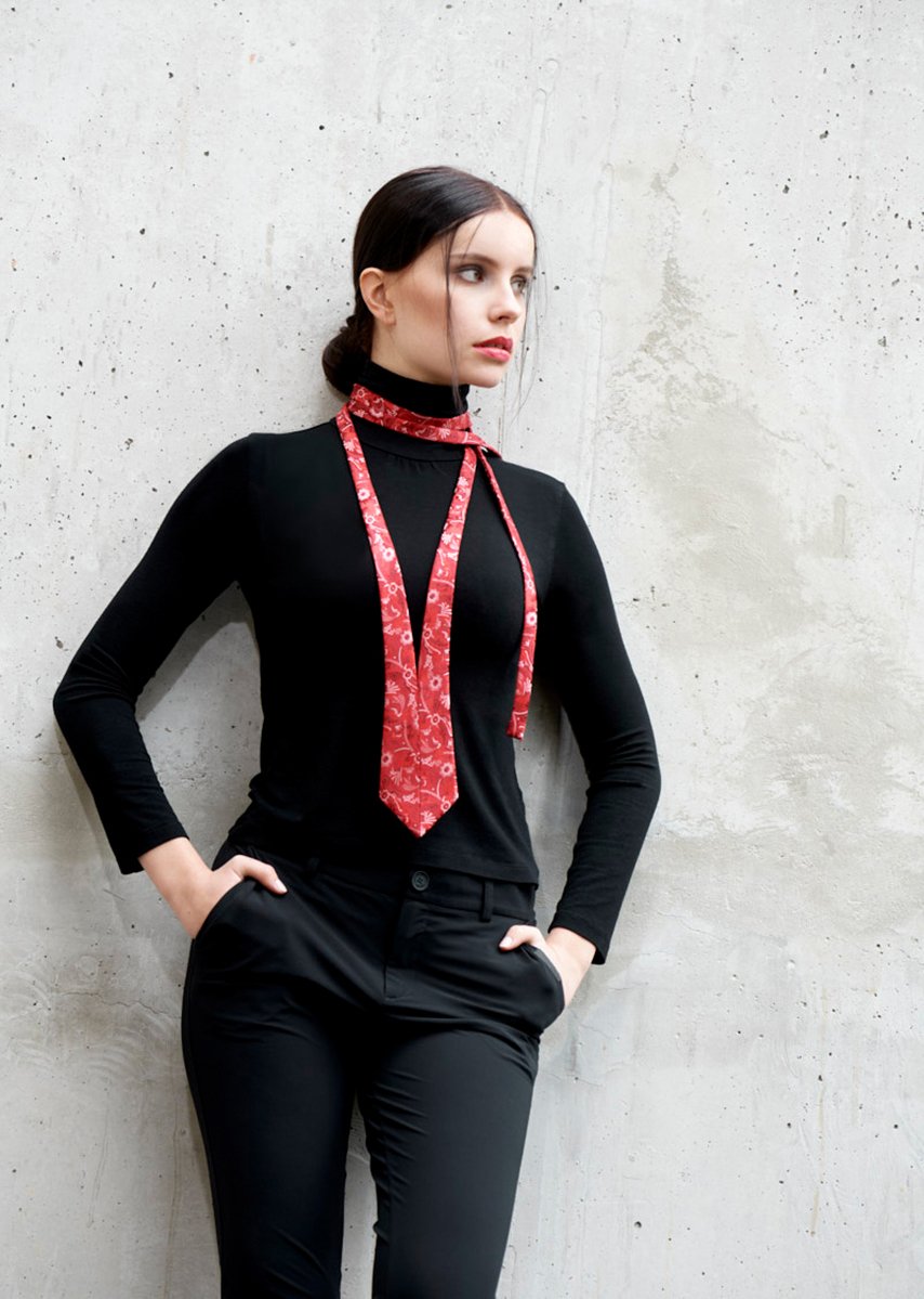 junge Frau in schwarzer Kleidung trägt eine rote Krawatte vor grauem Beton