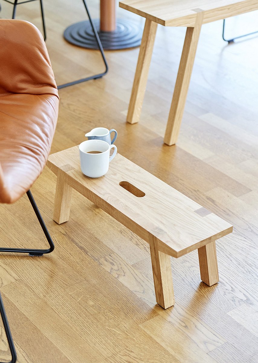 schmale, elegante Holzbank in Ambiente mit Kaffeetasse.Small wooden bench in ambience with coffee cup.