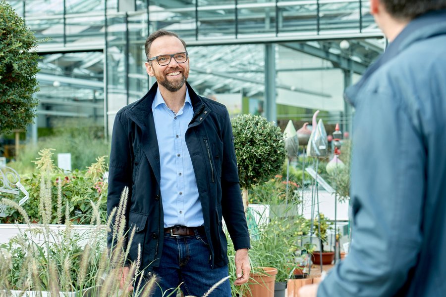 freundlicher, männlicher Versicherungsvertreter mit Brille in Beratung mit einem Gärtner in seiner Gärtnerei
