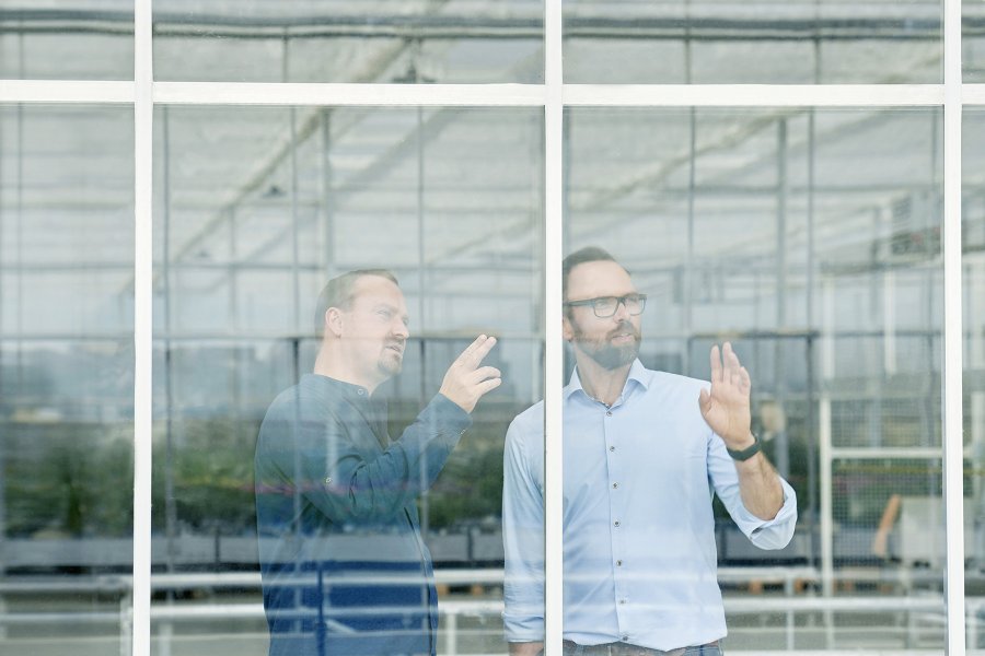 Zwei Männer schauen durch ein Gewächshausfenster nach draußen