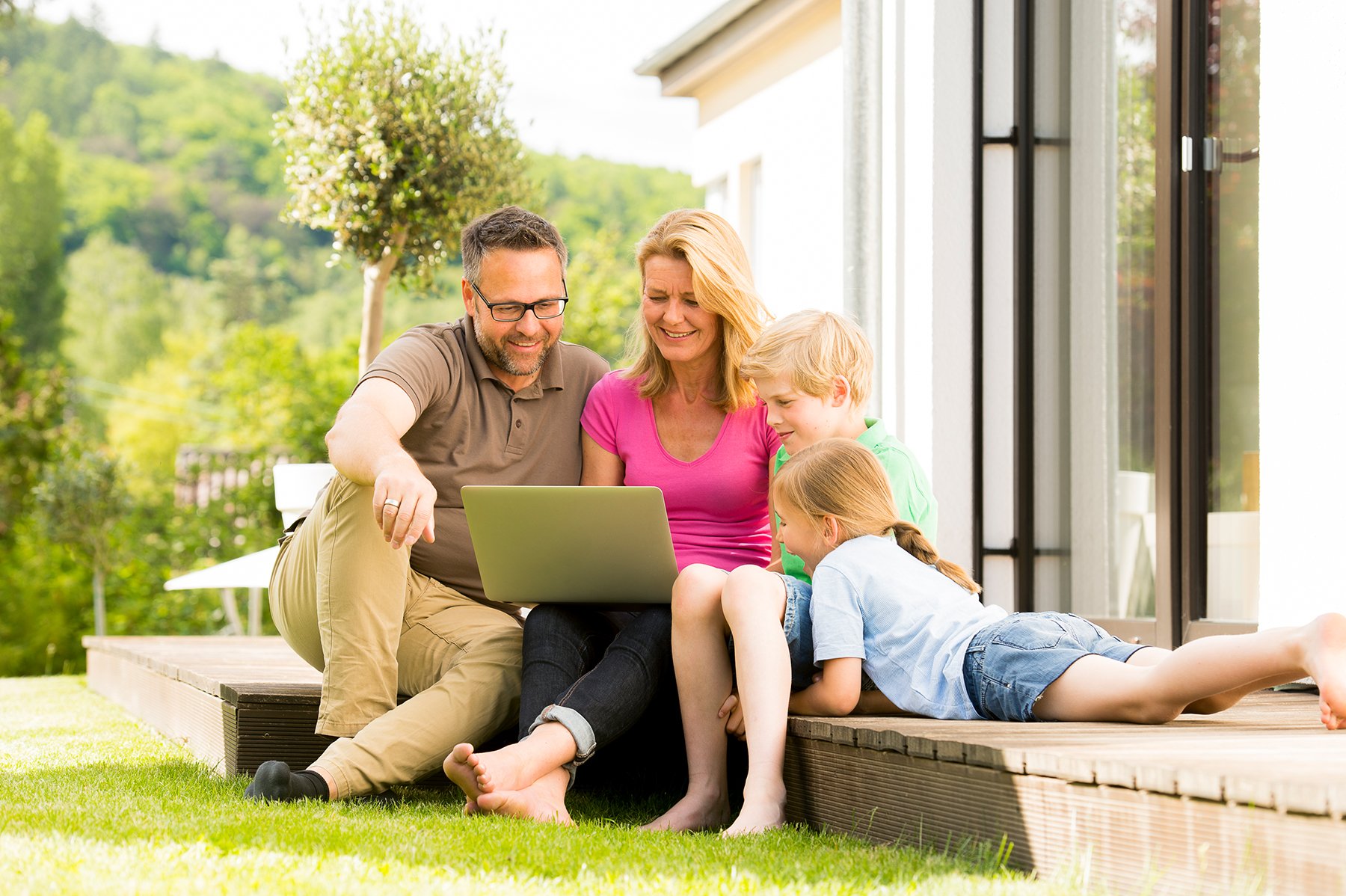 Famile sitzt im Garten und liest im Laptop die Tageszeitung der AZ